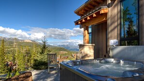 Un jacuzzi con revestimiento de madera, un pilar de piedra y vistas a montañas y árboles.