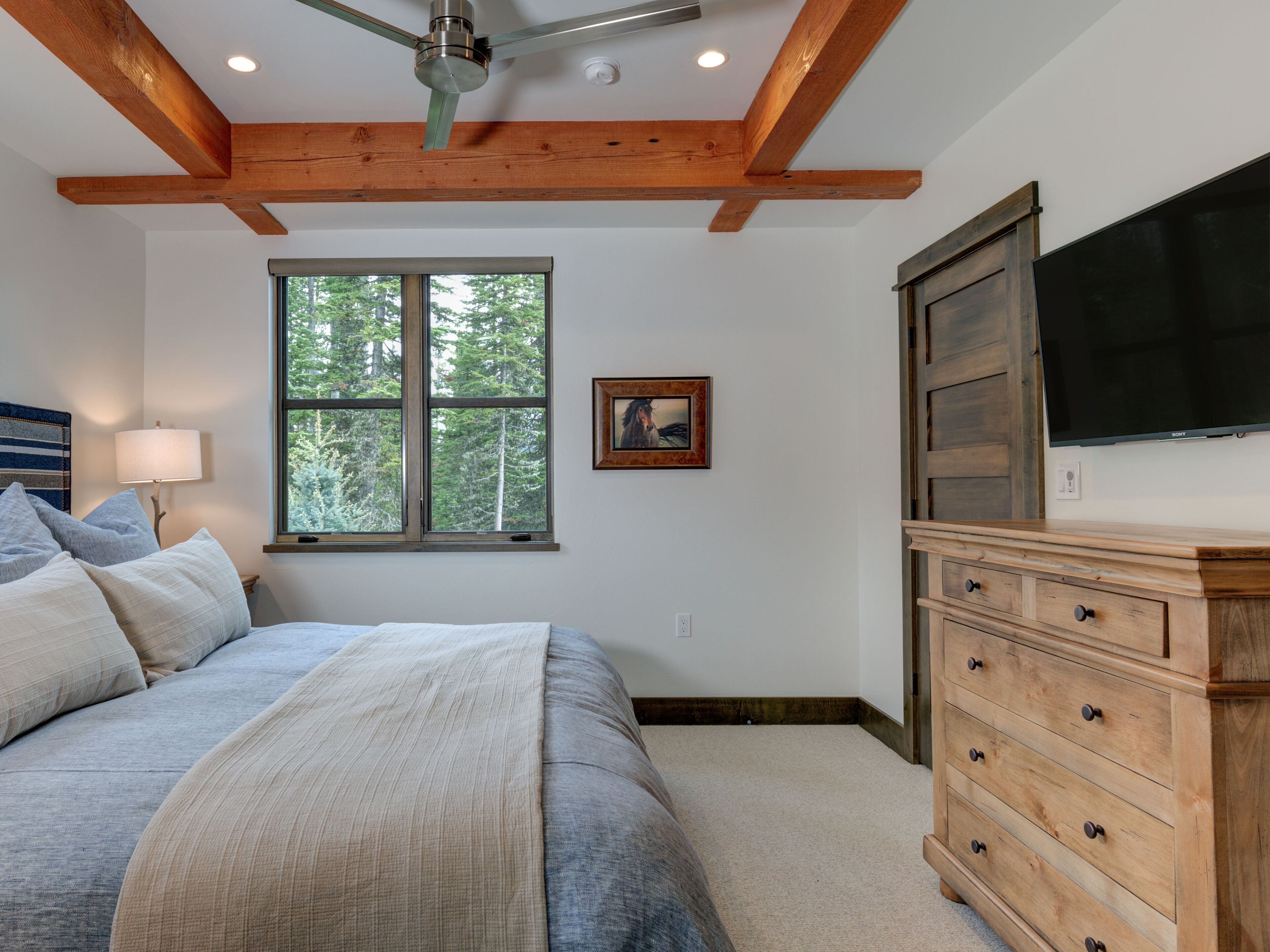 A bedroom with a bed, a dresser, a TV, a window, and a ceiling fan.
