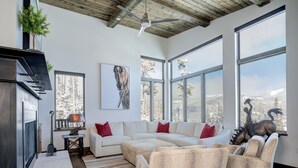 Amplia sala de estar con sofá modular, chimenea y ventanas grandes que ofrecen vista a un paisaje nevado.
