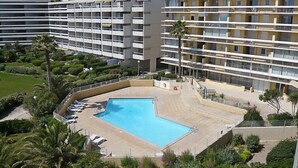 A modern hotel with a central swimming pool surrounded by lush greenery and palm trees. - Copacabana by Interhome (Canet-Plage)