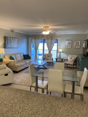 A living room with a glass-top dining table, a sofa, a chair, and a ceiling fan.