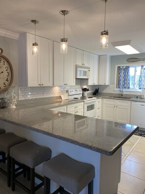 A modern kitchen with white cabinets, a granite countertop, and pendant lighting.