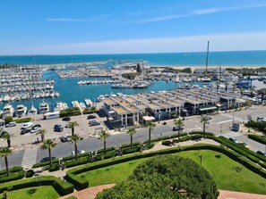 Un port de plaisance où sont amarrés de nombreux bateaux, un parking et une route bordée de palmiers.