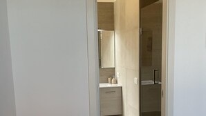 A hotel room with a bed, a desk with a lamp, a bathroom with a mirror, and a shower area.