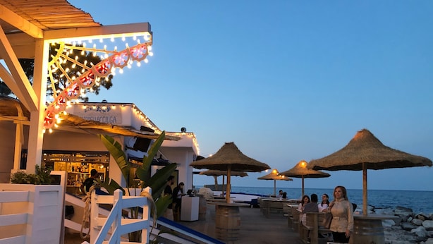 Een houten terras met rieten parasols, een bar en uitzicht op de zee.