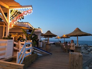 Eine Holzterrasse mit reetgedeckten Sonnenschirmen, einer Bar und Meerblick.
