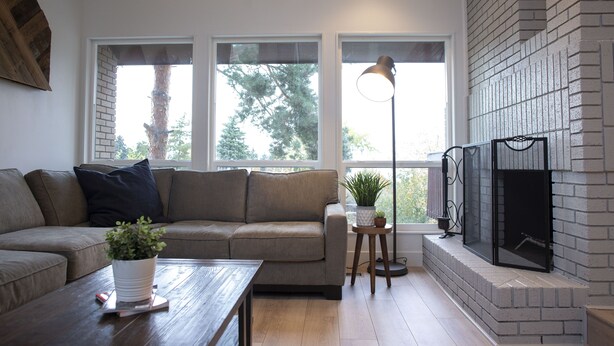 Ein Wohnzimmer mit einer Couch, einem Couchtisch mit einer Pflanze, einem Kamin und großen Fenstern.