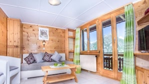 Una habitación acogedora con detalles de madera, un sofá con cojines, una mesita y una ventana con cortinas.