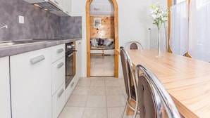 Cocina moderna con armarios blancos, una mesa de comedor de madera y vista a una zona de estar acogedora a través de un arco.