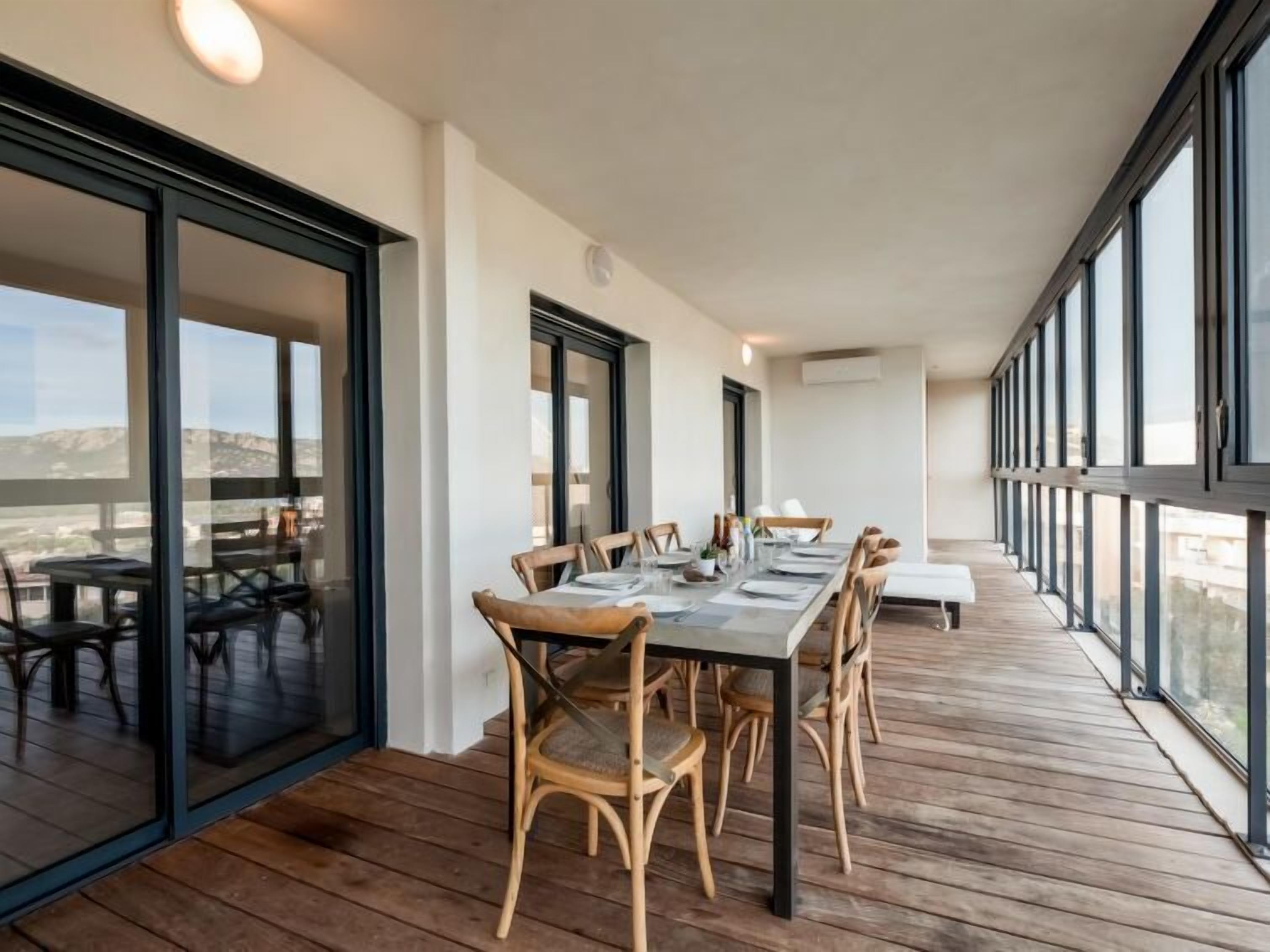 Un balcón amplio con una larga mesa de comedor dispuesta para seis personas, rodeado de sillas de madera.