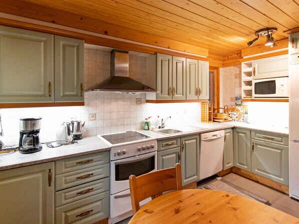 A kitchen with light green cabinets, a stainless steel range hood, a white stove, a microwave, and a wooden dining table.