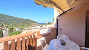 A balcony with a table and chairs, overlooking a coastal town and hills. - Terrazza Cala Rossa by Interhome (Nisporto)