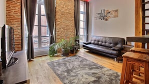 A living room with a brick wall, a leather sofa, a wooden coffee table, a TV, and a large window with curtains.