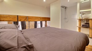 A modern bedroom with a large bed, a wooden headboard, a shower, and a bathroom with a sink and mirror.