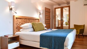 Un dormitorio ordenado con un cabecero de madera, una mesita de noche con un libro, una silla verde y un espejo al fondo.