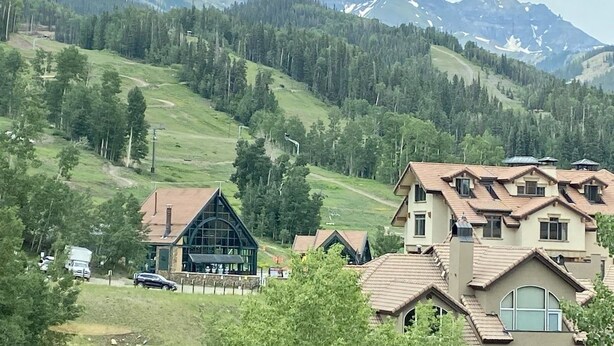 Un barrio residencial con casas, una colina verde y montañas al fondo.