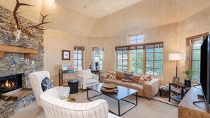 Un salón amplio con chimenea de piedra, asientos cómodos y ventanas grandes.