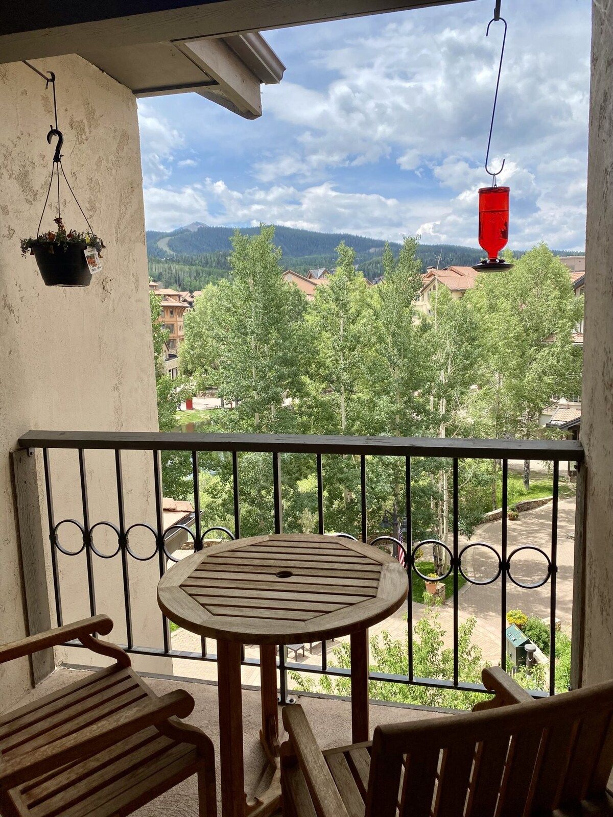 Ein Balkon mit einem runden Holztisch und zwei Stühlen mit Blick auf eine Wohngegend mit Bäumen und Häusern.