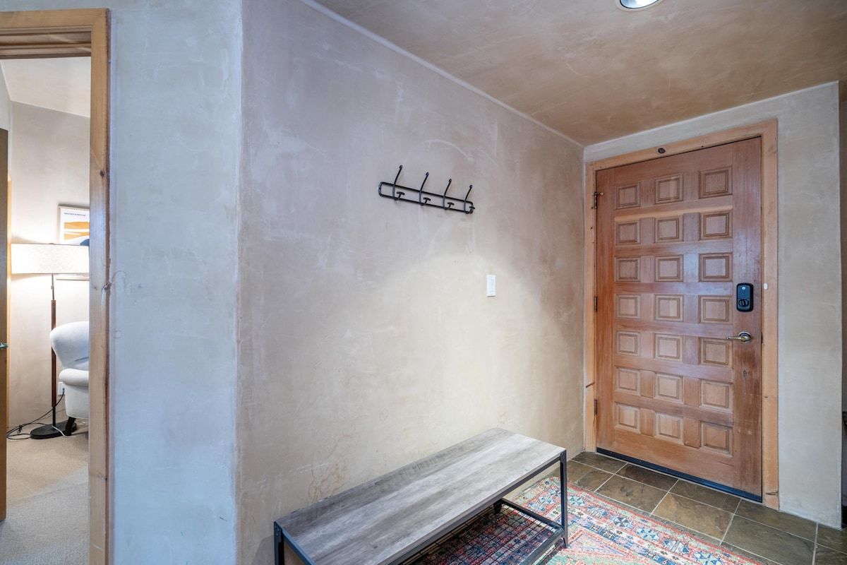 A hallway with a wooden bench, a coat rack, and a door with a keypad lock.