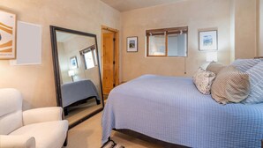 Un dormitorio con cama, una silla, un espejo y cuadros en la pared.