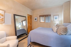 Une chambre à coucher avec un lit, une chaise, un miroir et des tableaux encadrés accrochés au mur.