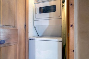 A compact, white washing machine installed in a wooden cabinet with a small window.