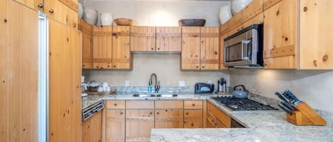Een keuken met houten kastjes, een magnetron, een gasfornuis en een spoelbak.