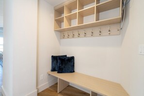 A hallway with a wooden bench, a coat rack, and a wall-mounted shelf.