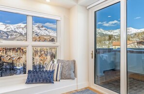 Ein Zimmer mit großem Fenster und Bergblick, einer Schiebeglastür und einer Sitzecke mit Kissen.