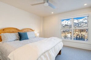 A bedroom with a bed, a ceiling fan, and a window with a mountain view.