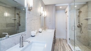 A modern bathroom with a glass-enclosed shower, a large mirror, and a white countertop with two sinks.