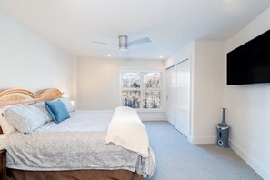 Une chambre avec un lit, un ventilateur de plafond, une fenêtre donnant sur un beau paysage et un téléviseur fixé au mur.
