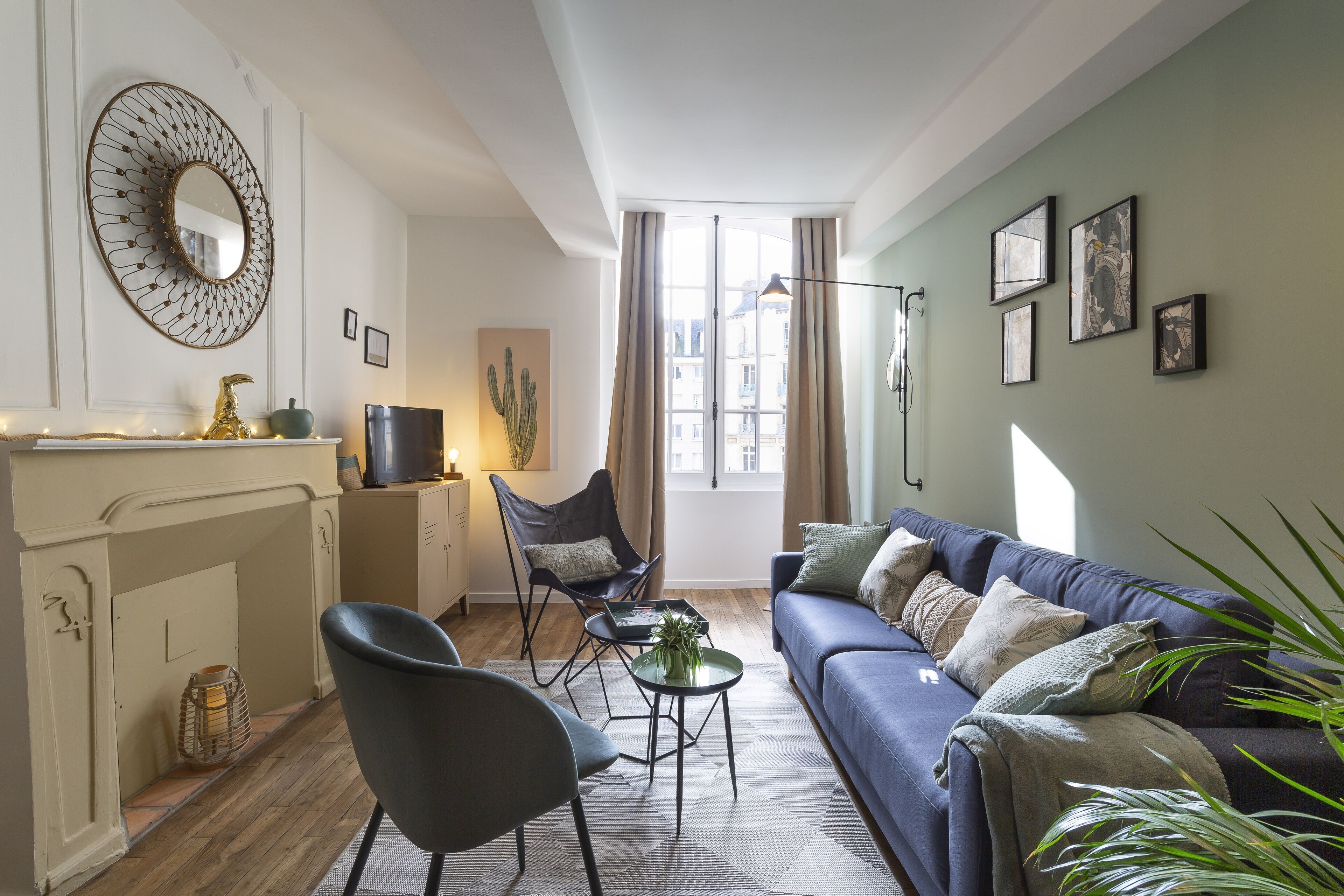 Un salon avec un canapé bleu, un fauteuil noir, une petite table ronde et une cheminée.