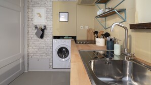 A compact kitchen with a washing machine, a sink, and a wooden countertop. - LE TOUCAN, 2 pièces de charme et emplacement de rêve - Parlement de Bretagne (Rennes)