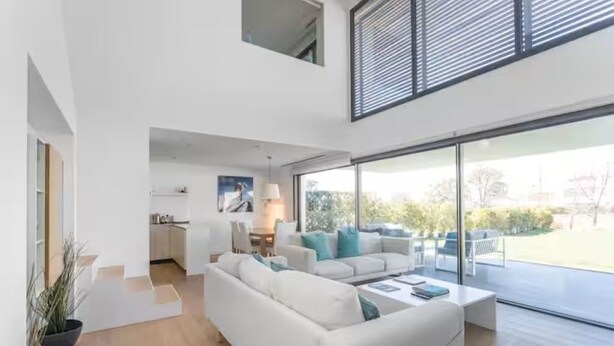 Un salón espacioso con un sofá blanco grande, una mesa de centro y vistas al exterior a través de puertas de vidrio amplias.