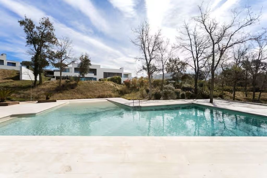 A swimming pool with a clear blue water, surrounded by a white deck and trees.