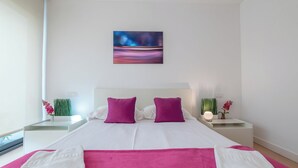 Una habitación de hotel moderna con una cama grande, dos mesitas de noche, un cuadro y una ventana.