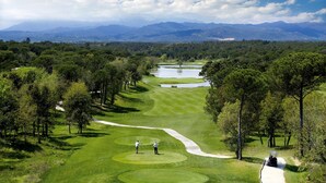 Campo de golf con una vista despejada del paisaje, incluyendo árboles y montañas distantes.