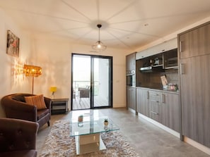 A modern living room with a glass coffee table, a sofa, and a dining area with wooden cabinets.