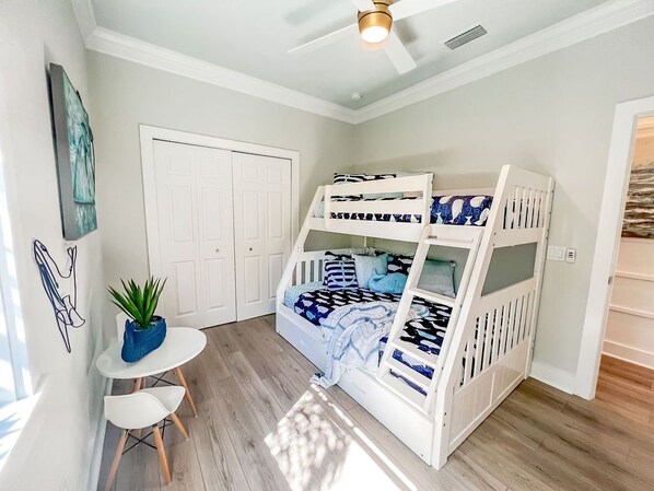A room with a bunk bed, a small table with chairs, a potted plant, and a ceiling fan.
