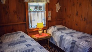 Une chambre de style cabine avec deux lits, une fenêtre avec des rideaux, une lampe sur une table et une décoration sur le thème de la marine.