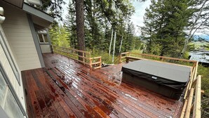 Una terrazza in legno con idromassaggio, circondata da alberi e una casa.