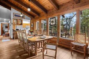 A wooden interior with a dining area, kitchen, and large windows offering a view of trees.
