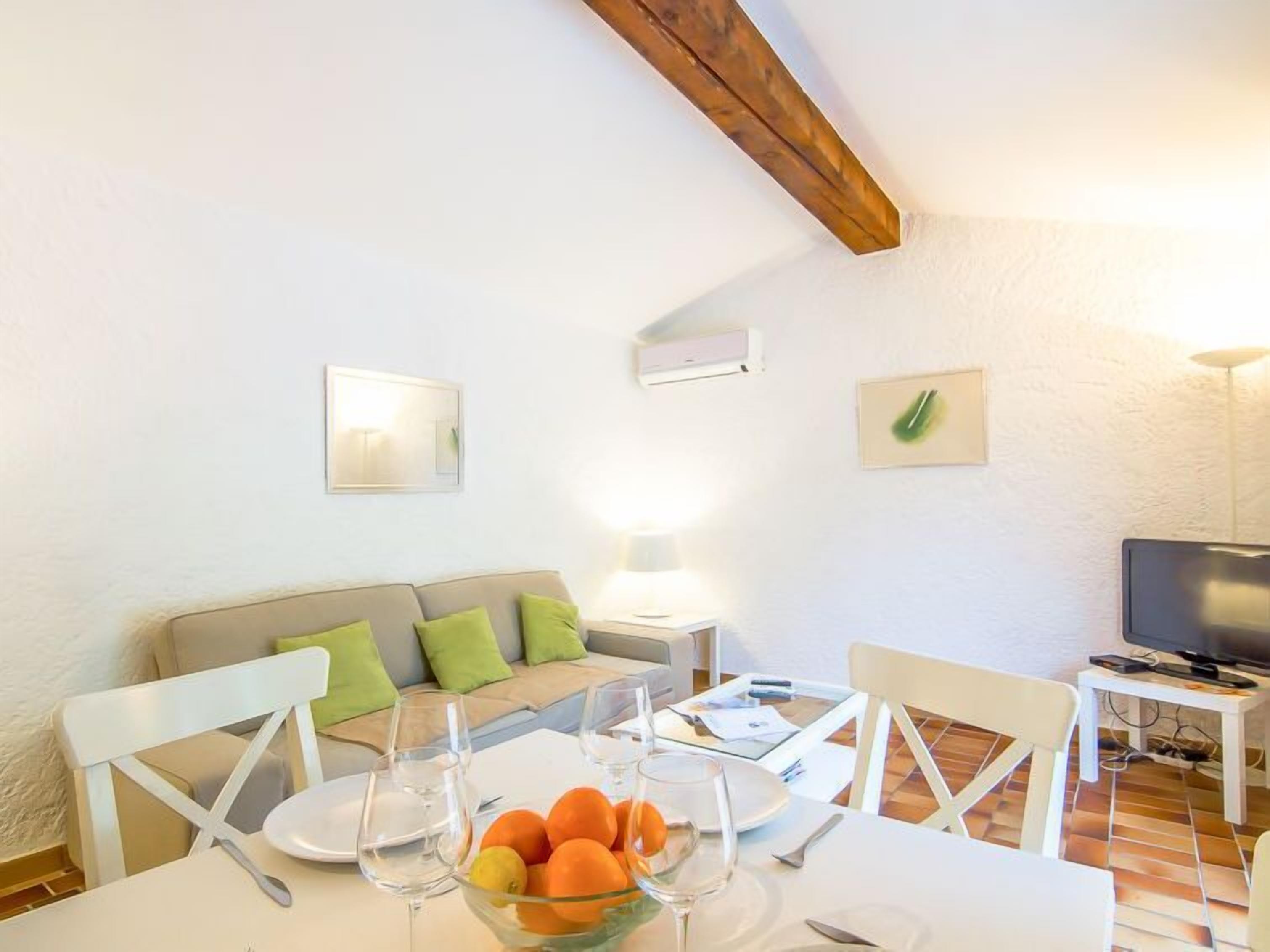 A dining area with a table set for two, a sofa with cushions, a TV, and a ceiling fan.