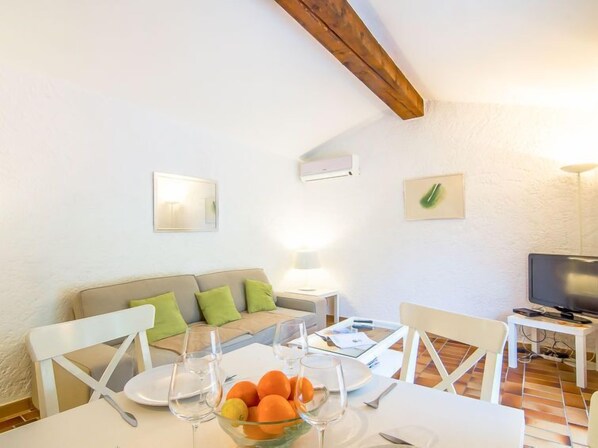 A dining area with a table set for two, a sofa with cushions, a TV, and a ceiling fan.