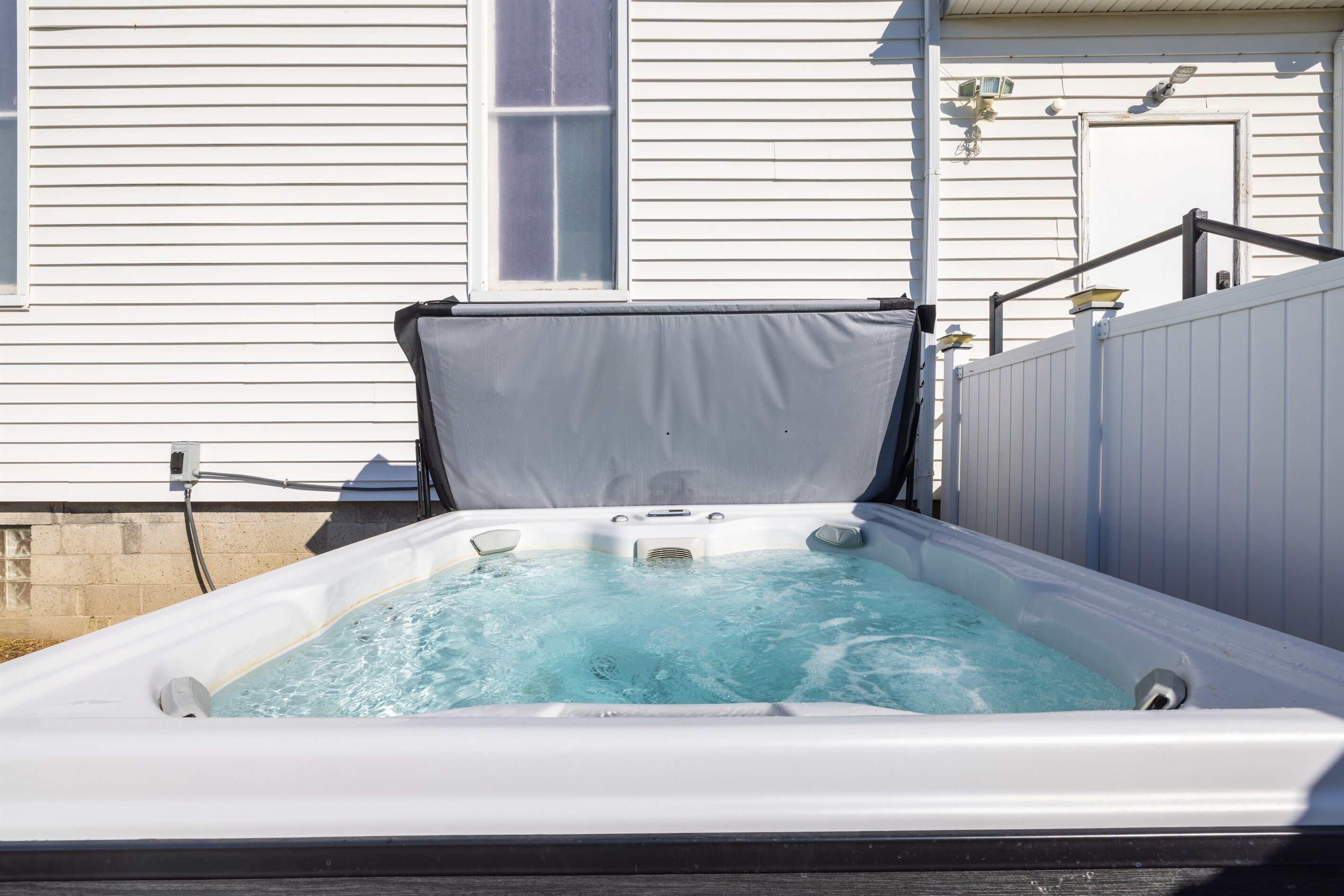 A hot tub with a mesh cover, positioned outdoors against a white house wall.