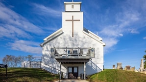 A white church with a cross on the front, a balcony, and a cemetery in the background. - The Sanctuary (Near Tecumseh) (Kingston)