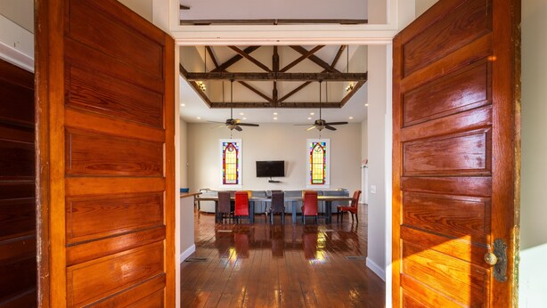 A wooden door leading to a room with a ceiling fan, a television, and a seating area with chairs and a table. - The Sanctuary (Near Tecumseh) (Kingston)