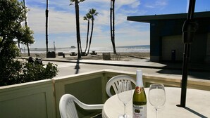A table with a bottle of Martini & Rossi sparkling cider and two glasses, overlooking a beach with palm trees and a pier. - A19 Lower Strand Cottage,10 secs to sand! Convenient location - corner of main rds (Oceanside)