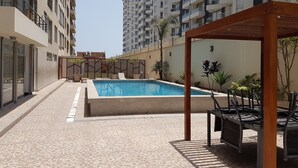 A swimming pool area with tiled flooring, a pergola, and outdoor seating.